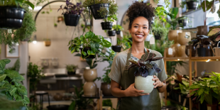 A woman in an apron holding a potted plant in a plant store.