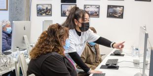 woman with face mask giving computer instruction to students sitting at desktop computers