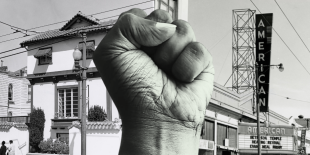 Black and white photo of a fist raised in the Black Power salute. In the background on the right a neon sign reading, &quot;American,&quot; above a marquee with the same name. On the left sits a white building with a tiled roof. 