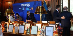 Color photograph of books on a table. Each book has an accompanying letter, with print too small to read. There's a blue sign in the background that reads, "EU and US: Stronger Together."