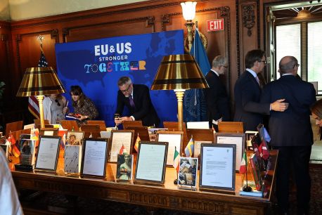 Color photograph of books on a table. Each book has an accompanying letter, with print too small to read. There's a blue sign in the background that reads, "EU and US: Stronger Together."
