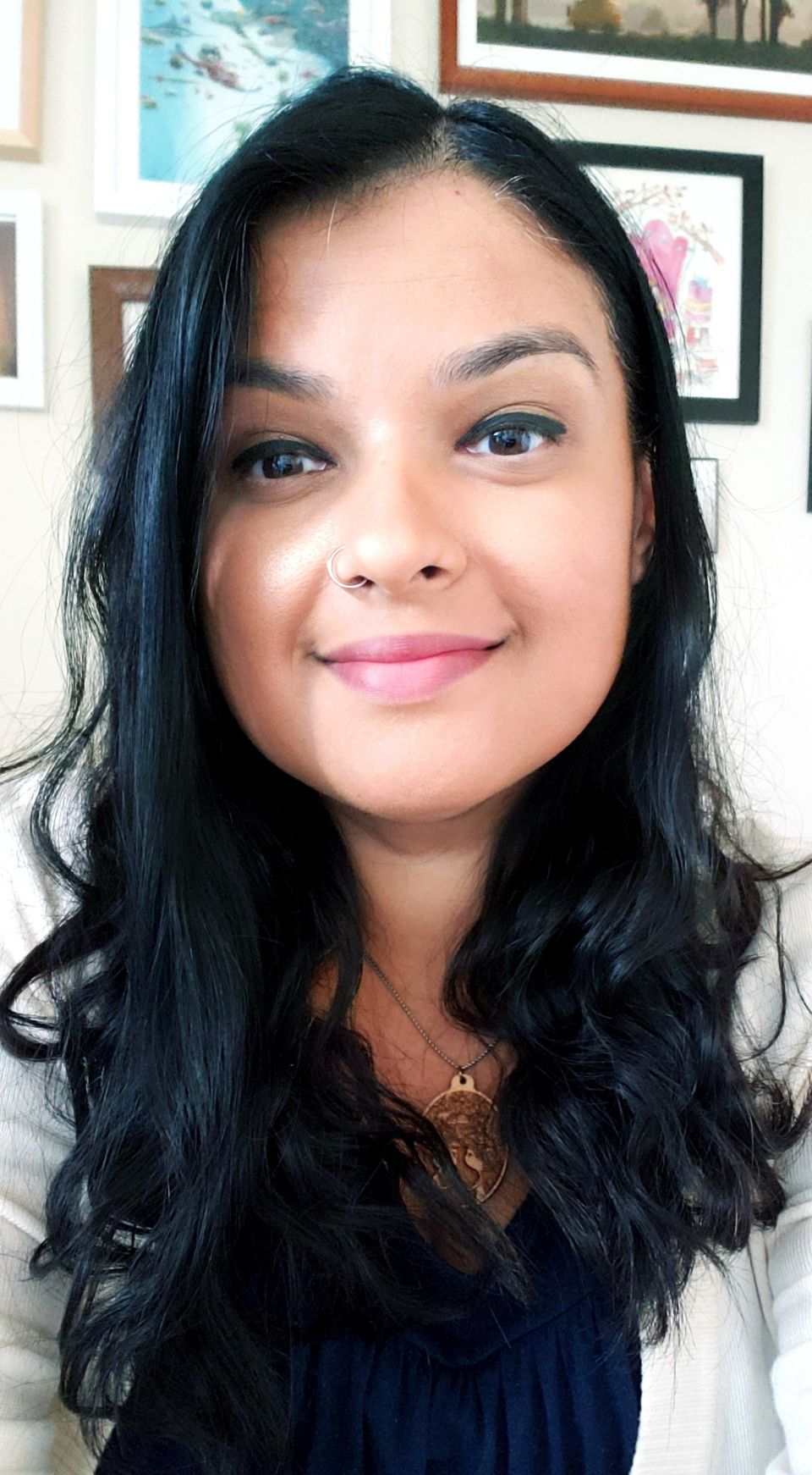 Woman with black curly hair wearing white cardigan and gold necklace