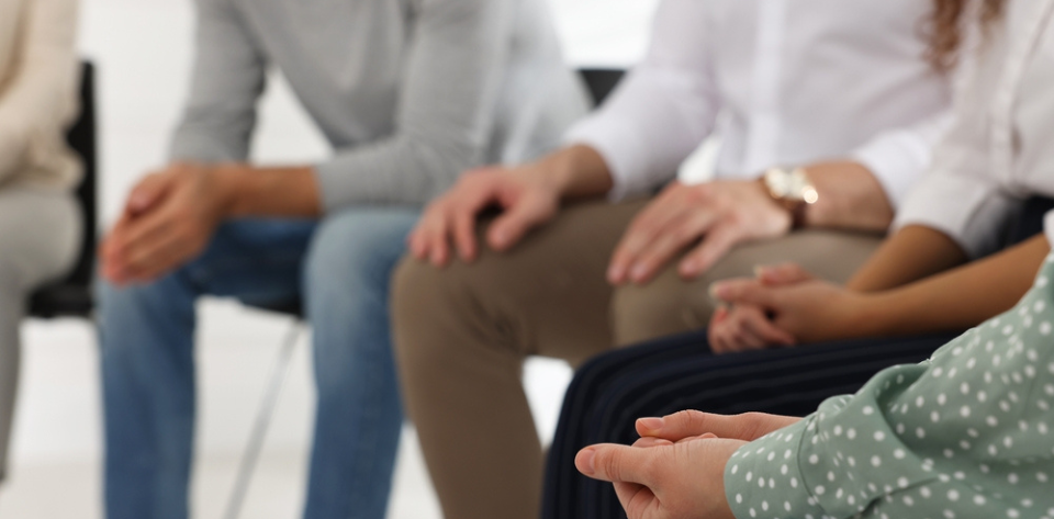 A group of people sitting in a circle seen from chest down with hands in their laps.