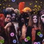 A photograph depicting a group of nine people in drag and heavy makeup, standing and looking into the camera.