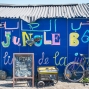 A photograph small structure with a corrugated metal roof, painted bright blue, with the words &quot;Jungle Books&quot; emblazoned colorfully on the side in Arabic, English and French. In front of the structure are a bike, a generator, and a chalkboard sign.