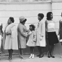 Black and white photograph of intergenerational Black women and girls standing and talking in front of a church.
