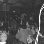 Black and white photograph of a band playing in a small venue. In the foreground, the lead singer is a woman with short, bleach blonde hair who is playing a guitar and screaming into a microphone. The bass player is standing behind the singer. There is a large audience of young punks surrounding the stage.